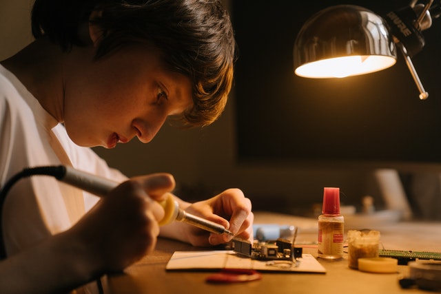 boy at desk using a soldering iron, neurodivergent